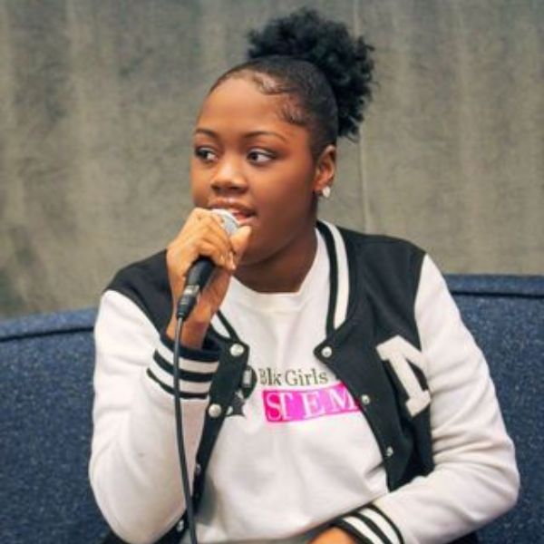A Black girl with her hair pulled back speaks into a microphone.