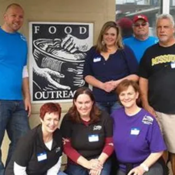 A group of smiling people near a sign that says, "Food Outreach."
